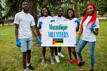 Group of happy african volunteers hold blank with Mozambique flag in park. Africa countries...