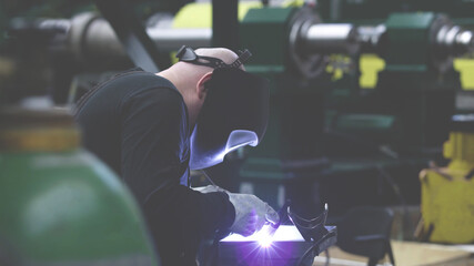 professional weld worker while using TIG Welding, wearing safety protective mask in selective focus view. Gas tungsten arc welding GTAW torch welder background - 399740412
