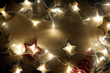 Dark Christmas and New Year frame template from christmas decorations illuminated by a led garland on light oak wood textured surface with copy space