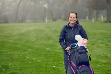 Happy friendly smiling female golfer with bag and clubs on a lush green golf course on a cold misty...