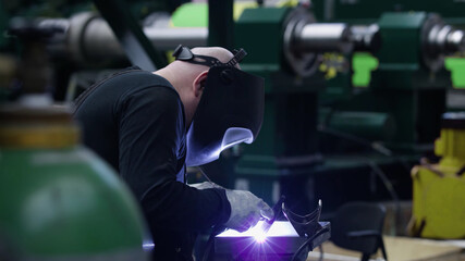 professional weld worker while using TIG Welding, wearing safety mask and protective clothing, selective focus background. Gas tungsten arc welding GTAW torch welder - 399740886