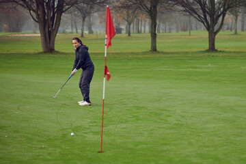 Middle-aged fit woman golfer putting for the hole on the green viewed from the flag as her golf...