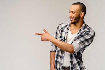 Joyful friendly african-american young man iwearing casual shirt pointing by finger at empty copy space