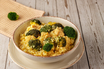 Creamy risotto with chicken and broccoli on wooden background