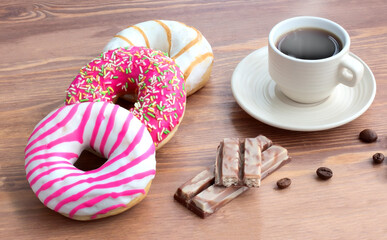 Glazed donuts, pieces of chocolate, hot coffee in a cup on the table.