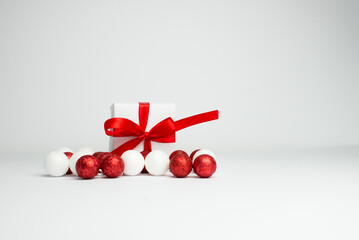 
Festive background. White gift with a red ribbon with white and red christmas balls on a white background. Gift box isolated on white background. Spece for text. Background for Christmas.