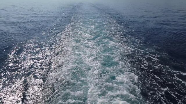Slow motion. Crane shot. White foam trail behind motor boat or ship. Water splatter behind ship stern.