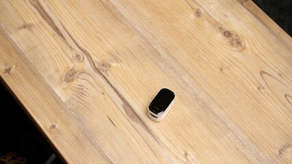 White heart rate monitor or oximeter with black screen lies on a wooden table or rough board....