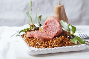 Italian large pork sausage cotechino served  with lentils on white plate.
