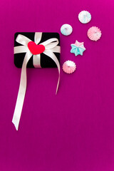Gift box with tape and heart and candy on a pink background. Copy space