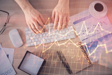 Multi exposure of man's hands typing over computer keyboard and forex graph hologram drawing. Top view. Financial markets concept.