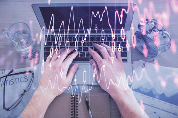 Multi exposure of man's hands typing over computer keyboard and forex graph hologram drawing. Top...
