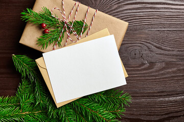 Christmas greeting card mockup with gift box and fir tree branches on wooden background