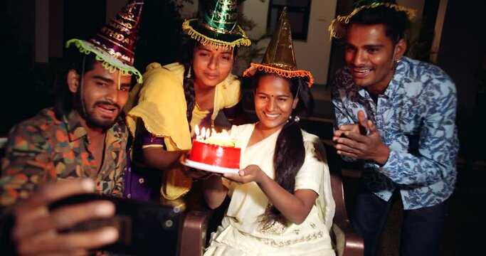 Slow motion handheld shot group of friends celebrate birthday party by lighting candles on cake for girl friend as they smile laugh enjoy take selfie photo on smart phone mobile sing dance