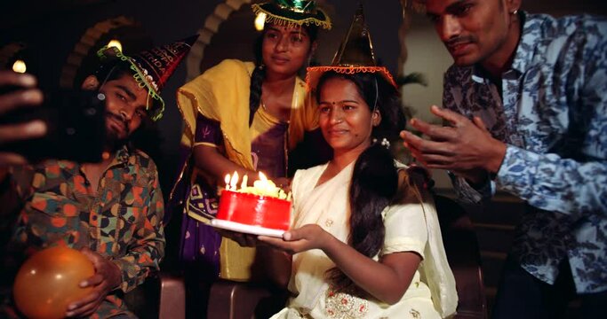 Slow motion handheld shot group of friends celebrate birthday party by lighting candles on cake for girl friend as they smile laugh enjoy take selfie photo on smart phone mobile sing dance