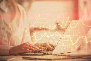 Double exposure of woman hands working on computer and forex graph hologram drawing. Financial...