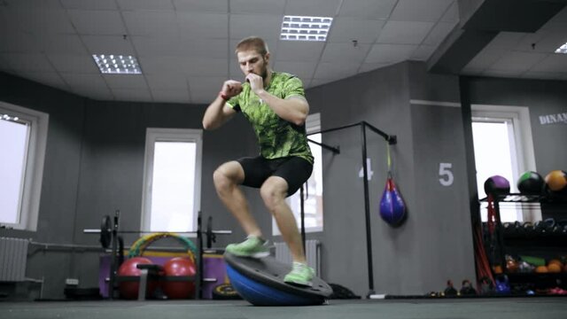 Energetic male athlete with strong body balancing on Bosu during active functional training in sports center 