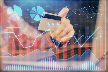 Double exposure of man hands holding a credit card and Forex graph drawing. Stock trading and digital fintech in Internet E-commerce concept.