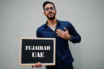 Arab man wear blue shirt and eyeglasses hold board with Fujairah UAE inscription. Largest cities in islamic world concept.