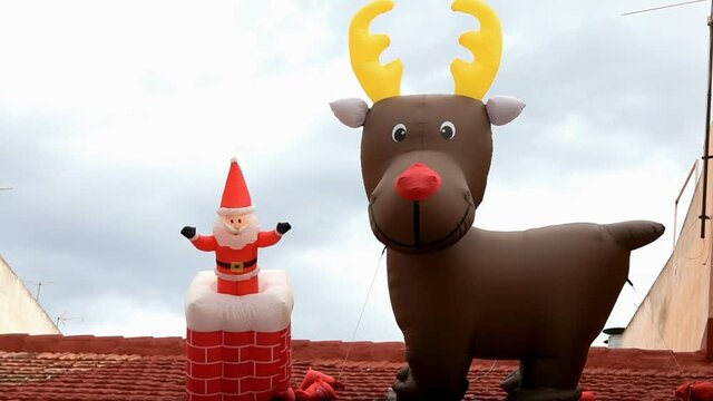 Footage of Christmas city decoration with giant Santa Claus and reindeer balloon characters on rooftop of a house. Funny holiday characters