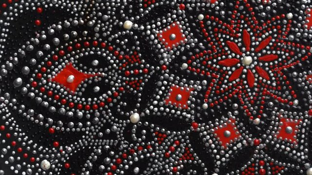 Decorative ceramic plate with red and silver colors, painted plate rotating on background, closeup, top view. Decorative porcelain plate painted with acrylic paints, handwork, dot painting