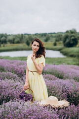 Fototapeta na wymiar Young beautiful woman in a yellow dress with a basket of flowers in a lavender field. Soft selective focus, art noise