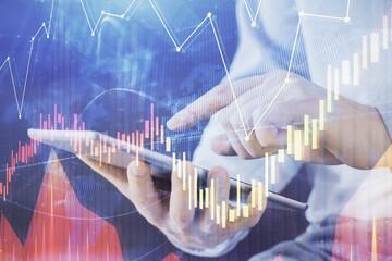 Double exposure of man's hands holding and using a digital device and forex graph drawing. Financial market concept.