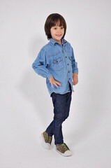 a small asian  boy in a denim shirt and full-length blue pants stands and stares straight ahead with his hands on his belt goes to the right