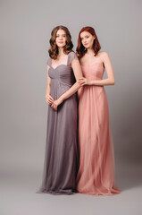 Two beautiful bridesmaids in long fashionable chiffon dresses posing in the studio. Full length...