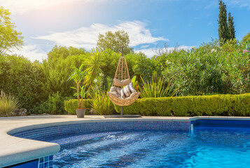 Luxurious pool in the garden of a private villa, hanging chair with pillows for leisure tourists, in summer. Portugal, Algarve.