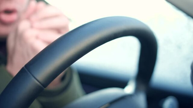 Male driver tries to get warm in a frozen car in cold winter morning