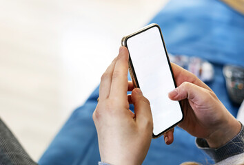 Caucasian woman hands holding a smart phone in a modern living room. White screen for copy space.
