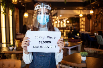 Distraught waitress temporarily closing cafe during coronavirus epidemic. Small business closing sign due to Covid-19 coronavirus. Barista holding closed sign