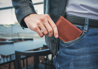 The man pulls a brown leather wallet out of his jeans pocket - obrazy, fototapety, plakaty