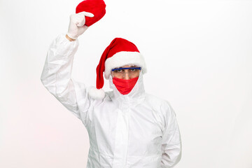Fototapeta na wymiar Health worker wearing protective clothing. He wears a santa hat on his head. He has a red corona mask on his face. He is holding a gift box in the shape of a heart.