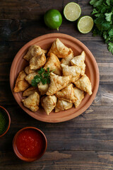Samosa - fried/baked pastry with savoury filling, popular Indian snacks, served in bowl with spices and fresh cilantro on rustic background