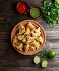 Samosa - fried/baked pastry with savoury filling, popular Indian snacks, served in bowl with spices and fresh cilantro on rustic background