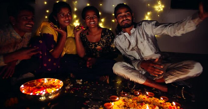 Slow-motion medium shot of friends, males and females, take selfie photo mobile smart phone camera technology Digital device during Diwali celebration decoration at home 