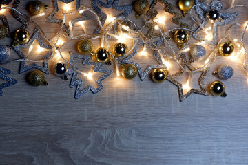 Christmas and New Year template with christmas decorations, gold and silver shiny, matte and sparkling christmas balls and garland of yellow led lights on light oak wood background with copy space