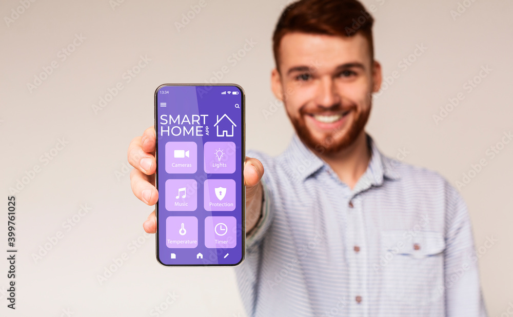 Poster happy millennial man showing mobile phone with smarthome automation control system on screen, white 