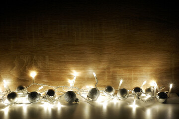 Dark Christmas and New Year composition from silver christmas balls illuminated by a led garland on light oak wood textured surface with copy space