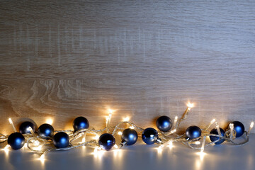 Christmas and New Year composition from blue christmas balls illuminated by a led garland on light oak wood textured surface with copy space