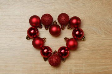 Heart from red shiny, sparkling, matte christmas balls on light oak wood textured surface