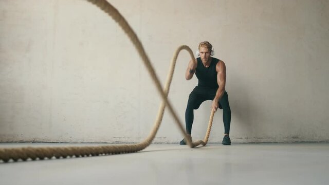 A determined sportsman is working out with battle ropes in the studio