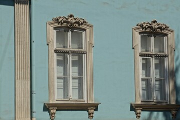 two large gray old windows on the blue wall of a historic building on the street