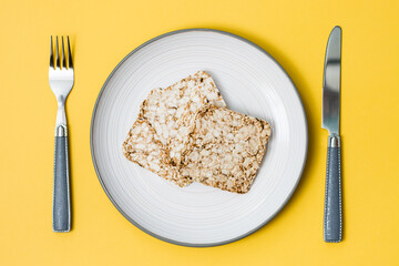 Healthy eating. Crispbread made from oats, wheat, flax and sesame seeds on a plate and cutlery on a yellow background. Top view