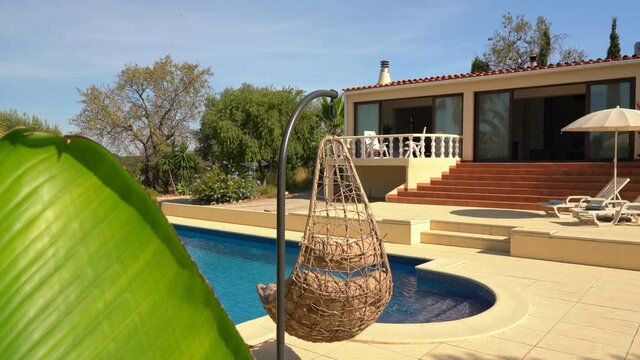Great view of the pool with sun loungers for tourists and clear water. Luxury villa , Palm leaf in the foreground.
