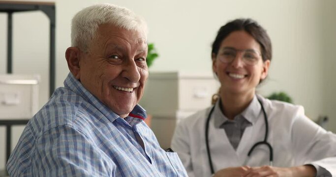 Older male patient and doctor on background smile looking at camera sit in clinic office. Portrait of satisfied hospital client, reliable high quality professional eldercare, medical insurance concept
