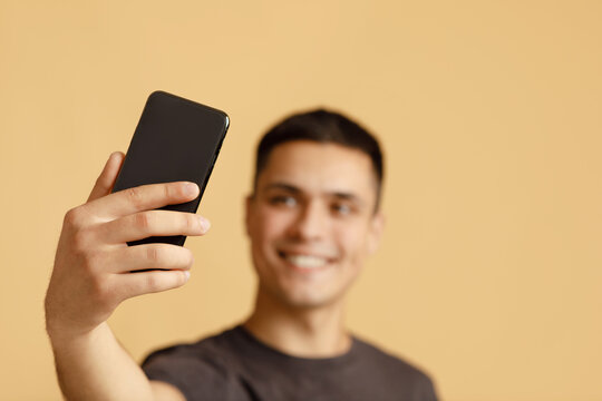 Smartphone in hand of smiling millennial guy blogger student, making photo