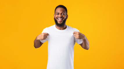 Cheerful Black Man Showing His White T-Shirt Over Yellow Background